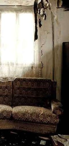 A fire-damaged room with a scorched wall and a soot-covered sofa beside a window