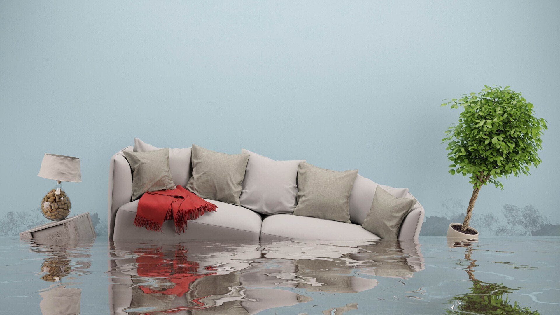 A flooded living room with a grey sofa and red throw standing in water